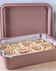 Pink baking pan with cinnamon rolls inside on a wooden surface